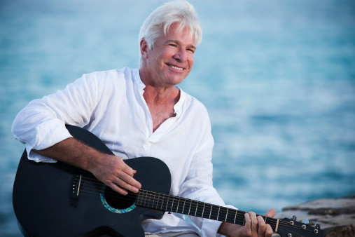 Attractive retired senior man in his 60's playing guitar on a beach vacation.