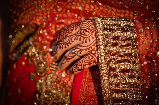 "Henna, mehendi on a womanaas hand. A traditional custom in the Asian and Arab world. Woman dressed in an intricate red bridal sari. Focus on sleeve."