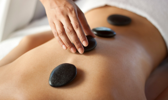 Hands massaging lower back with warm stones. You may also like: