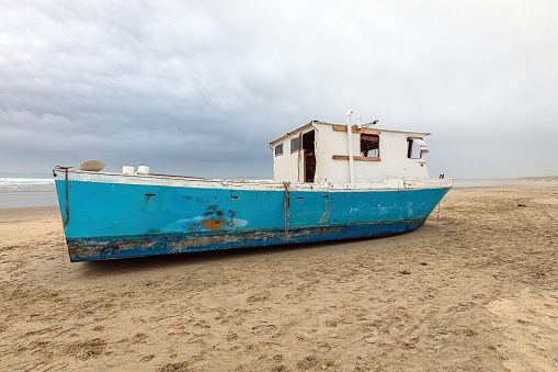 Old, abandoned fishing boat marooned on a sand beach on the central Oregon seacoast with storm clouds.