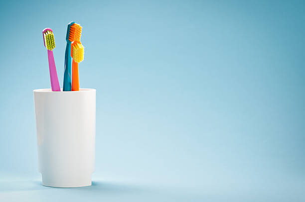 Three colourful soft toothbrushes in white mug on blue background stock photo