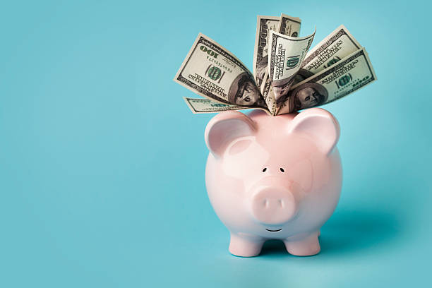 Pink piggybank stuffed with dollar bills "A smiling pink piggybank stuffed with $100 dollar bills, on blue background with copy space.  You may also like:" abundance photos stock pictures, royalty-free photos & images