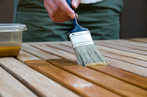 Woman Applying Stain to Wood woman using a paintbrush to apply a wood sealant on a patio table top wood stain stock pictures, royalty-free photos & images