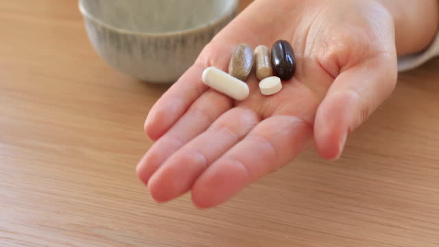 A woman pours a variety of pills or vitamins into her palm. Dietary supplements