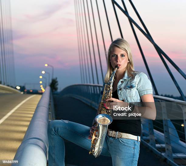 Joven Mujer Tocando El Saxofón En Iluminado Puente De Tirantes Al Atardecer Foto de stock y más banco de imágenes de 20-24 años