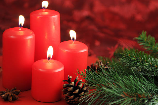 Four red Advent candles are burning. Aside laying pine cone and twig with star anise. On table with red tablecloth. Soft focus on first candle. Useful Christmas background for greeting card.