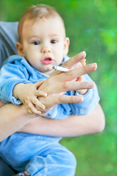 A little baby behind a hand with a lighted cigarette Smoking father holding baby. vibrant color lifestyles vertical close up stock pictures, royalty-free photos & images