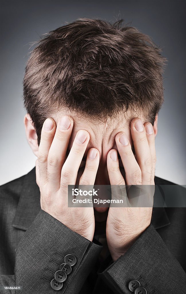 Hiding From Business Problems Young businessman expressing his emotional despair and covering his face with his hands. People and emotions concept. Adult Stock Photo