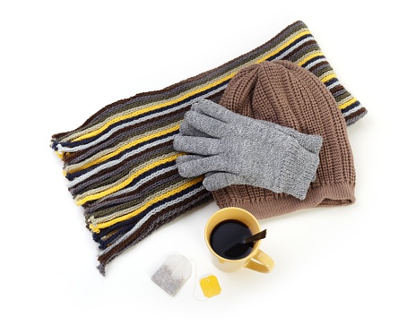 A cup of dark tea, teabag, scarf, warm hat and gloves. Isolated on white.