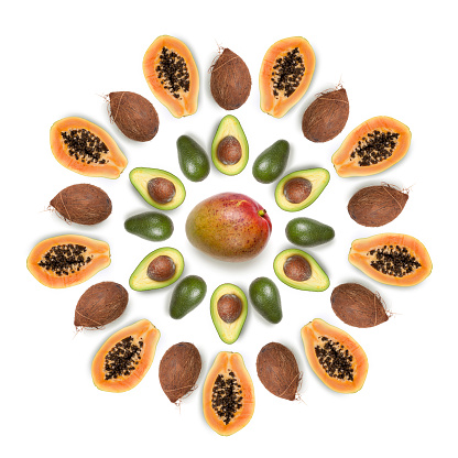 Composition made with various tropical fruits arranged into a sun shaped circular arrangement on white background: mangos, papayas, coconuts and avocados.