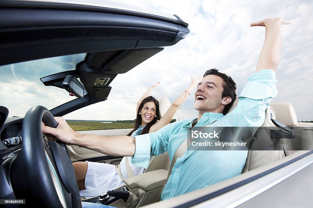 Hermosa pareja sentada en un descapotable coche con aumento de las manos. - Foto de stock de Adolescente libre de derechos
