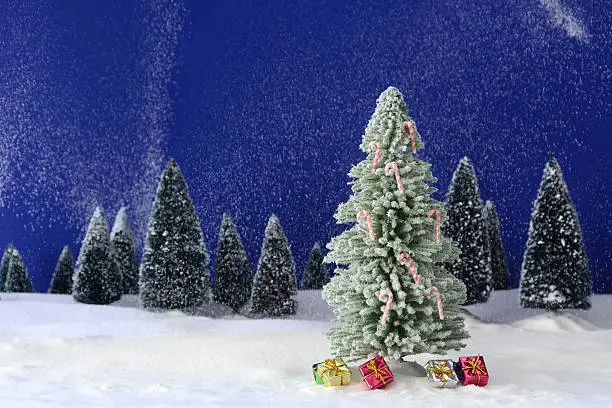 "A miniature diorama of a Christmas tree at dusk, decorated with candy canes, surrounded by presents, in a wintry landscape."