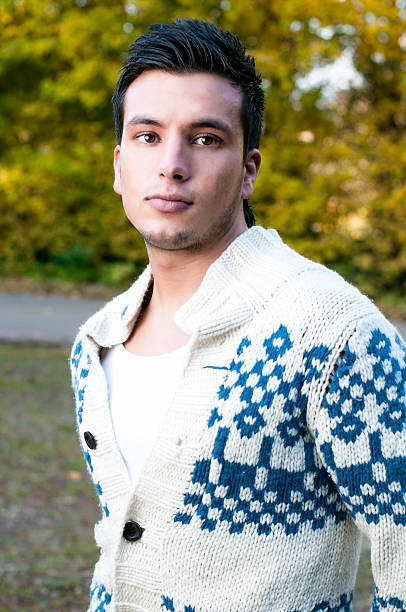 Young man looks away. He is not smiling and wearing a trendy knitted sweater.