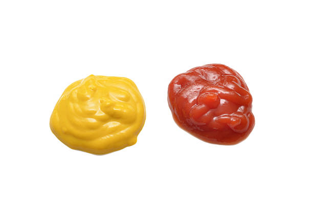 Close up of mounds of mustard and ketchup side by side on a white background.  