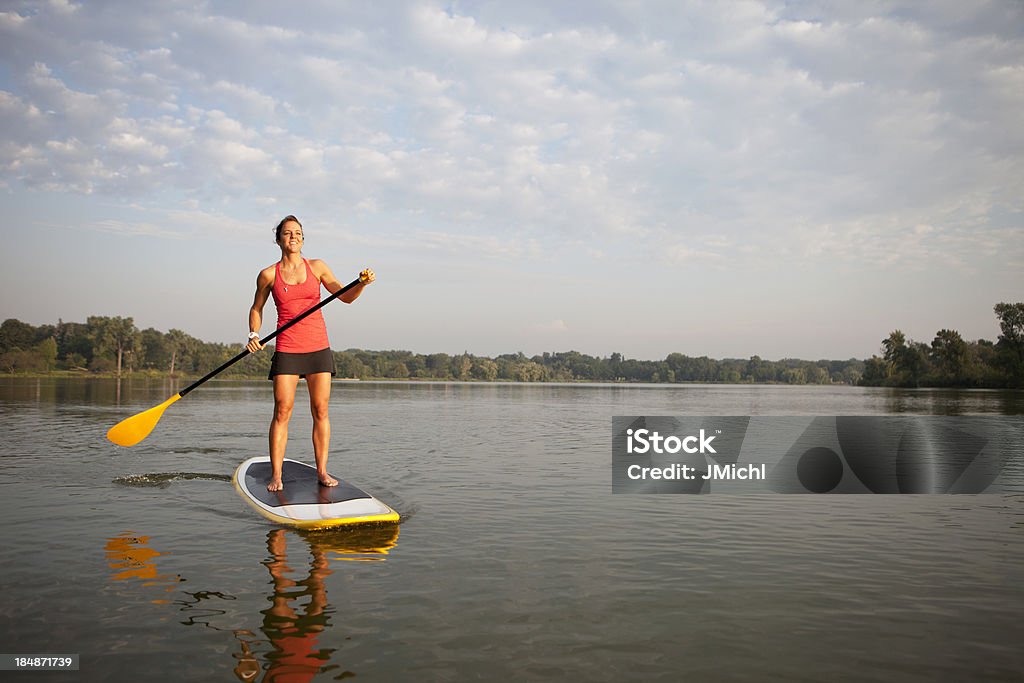 Kobieta z paddle stoi na paddleboard w wodzie - Zbiór zdjęć royalty-free (Paddle Surfing)