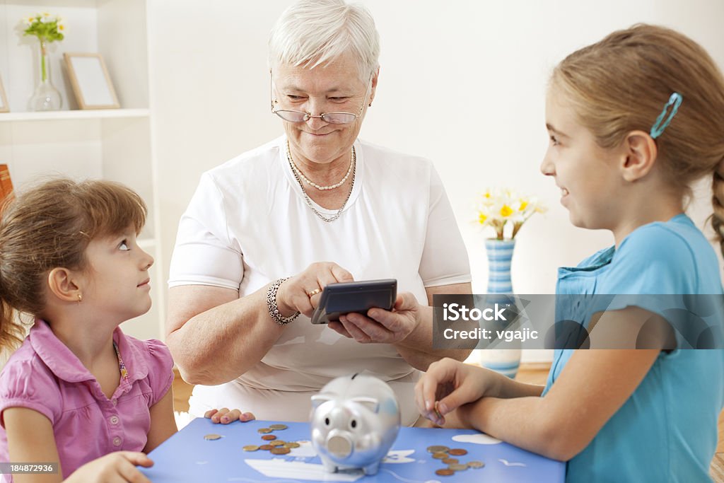 Nonna con i suoi nipoti conta soldi nel Salvadanaio a porcellino - Foto stock royalty-free di Donne anziane