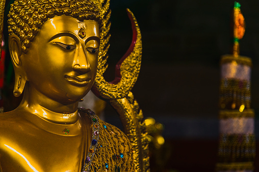 This close-up image captures the serene and intricate details of a gilded Buddha statue in Luang Prabang. The Buddha's facial expression exudes peace and contemplation, highlighted by the soft glow of the surrounding lights. Adorned with a complex headdress and jeweled ornaments, the statue embodies the rich cultural heritage and religious artistry of Laos.