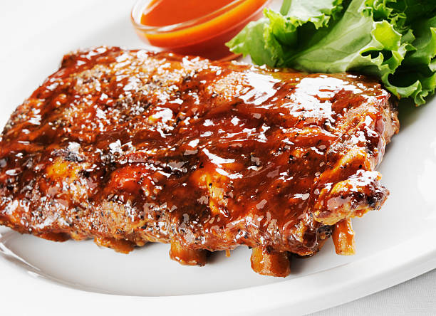 Juicy barbecue ribs Juicy barbecue pork ribs with lettuce and barbecue sauce in a white plate on a white background. barbecue pork stock pictures, royalty-free photos & images