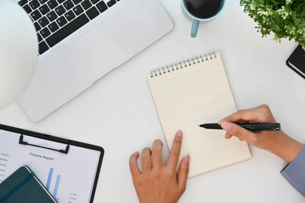 istock Above view of businesswoman working on laptop computer and writing notes in notebook 1848755679