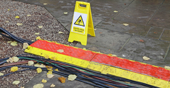 A trip hazard plastic sandwich board warning of cables running across a public path