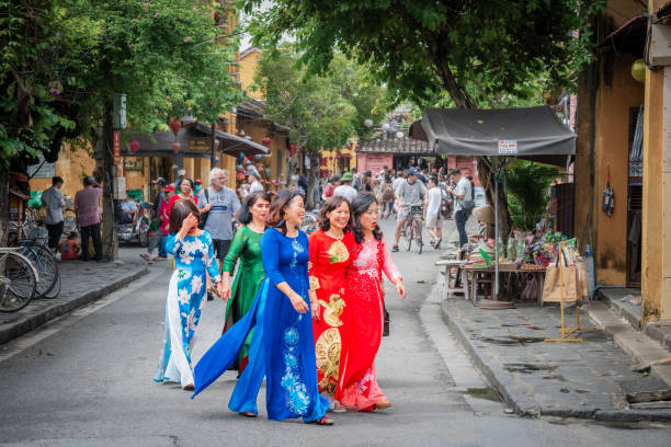 Hoi An, Vietnam, November 20, 2022: A group of Vietnamese women in traditional dresses walking on a busy street in Hoi An, Vietnam