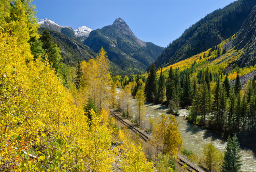Animas River Scenic Landscape Silverton to Durango Railroad.  Scenic area along the Animas RIver with narrow-gauge train tracks in steep rugged mountain canyon.  Scenic route with autumn fall colors and sunny blue-sky day.  Captured as a 14-bit Raw file. Edited in ProPhoto RGB color space.