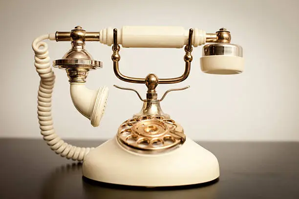"Slightly desaturated color image of an antique, Victorian-style rotary telephone sitting on a table."