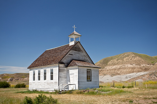 Old white church. Horizontal colour image. Historic white clapboard church in the badlands of Alberta. Church is in the ghost town of Dorothy, near Drumheller. Nobody is in the image, taken with Canon Mark II 5D body. Clear, hot, summer day on the prairie. 