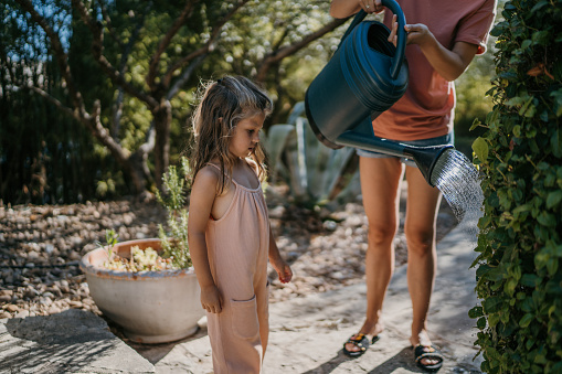 Mother watering plants with her daughter outdoors in back yard.