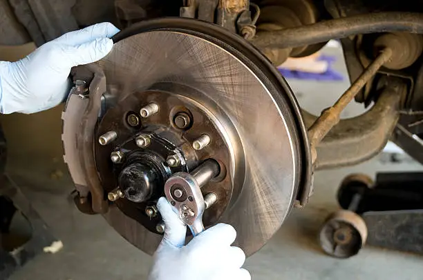 mechanic using a socket wrench to remove the bolts holding on the disc brake rotor and wheel hub