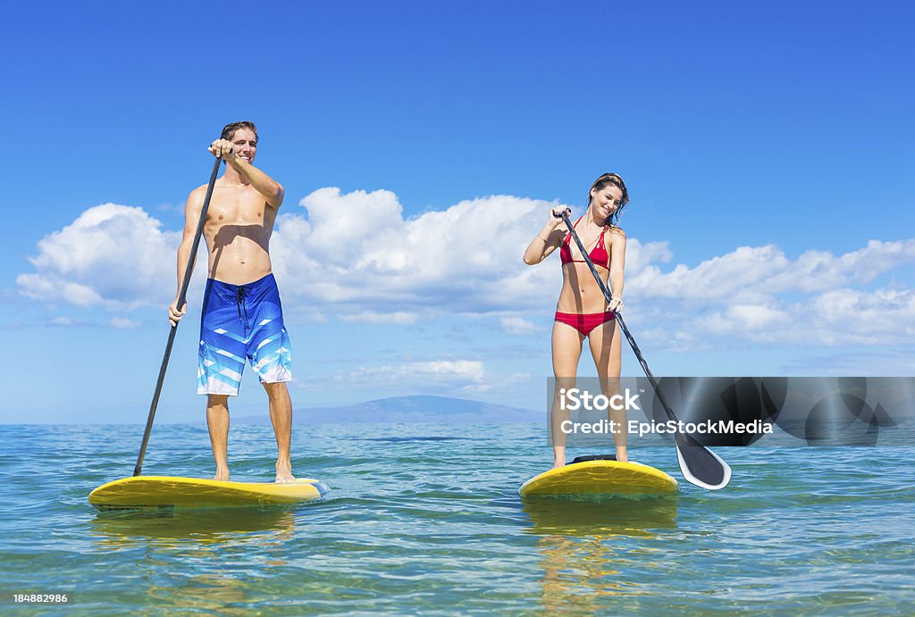 Couple Stand Up Paddle Surfing In Hawaii Couple Stand Up Paddle Surfing In Hawaii, Beautiful Tropical Ocean, Active Beach Lifestyle Paddleboard Stock Photo