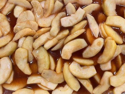 Close-up view of sliced apples in a sweet cinnamon sauce being prepared for baking into an apple pie.