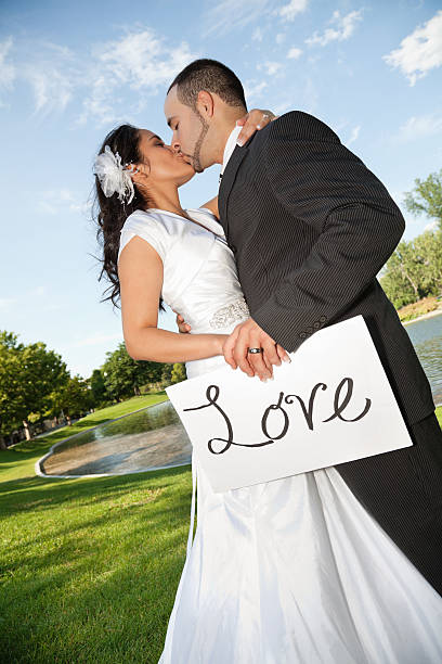 Bride and Groom Kissing While Holding Love Sign.
