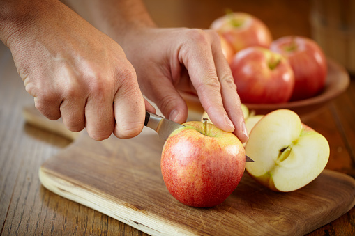 Hands slicing gala apples with bowl of apples in background, shot with shallow focus on hands and front apple.