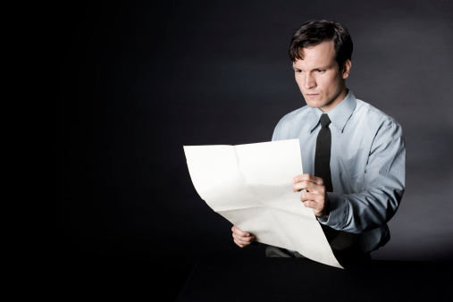 Business man reading newspaper. Man wearing shirt and necktie is reading a blank sheet of paper. Business man reading an empty newspaper. Vintage style. Black background. Low key. Studio shot. XXXL (Canon Eos 1Ds Mark III)