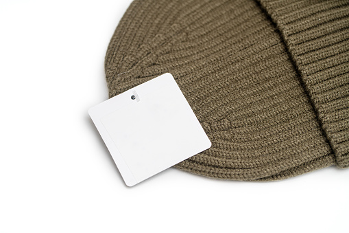 Brown knitted hat and blank clothing tag isolated on white background