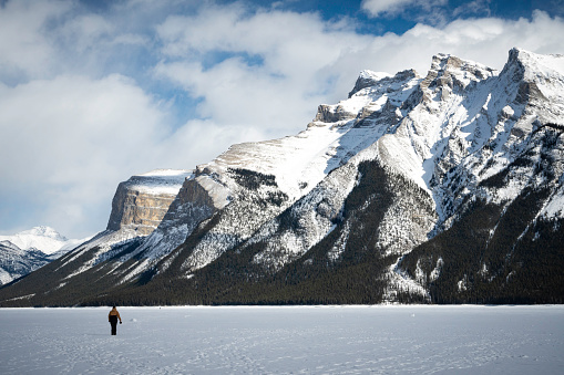Banff, Alberta, Canada - March 15, 2023: Tourists enjoy walking across the snowy frozen Lake Minnewanka on a winter day.