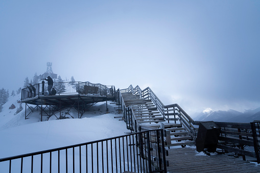 Banff, Alberta, Canada - March 26, 2023: Two people at the viewpoint platform at the Cosmic Ray Station on Sanson's Peak, Sulphur Mountain  at Banff Gondola on a very foggy day with no view of the valley below.