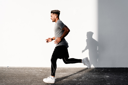 Keeping fit Maori man jogging in Auckland city against the while wall background.