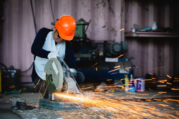 istock Heavy Industry Engineering Factory Interior with Industrial Worker Using Angle Grinder and Cutting a Metal Tube. Cutting metal and steel with a combination circular saw with a sharp round blade. 1848957138
