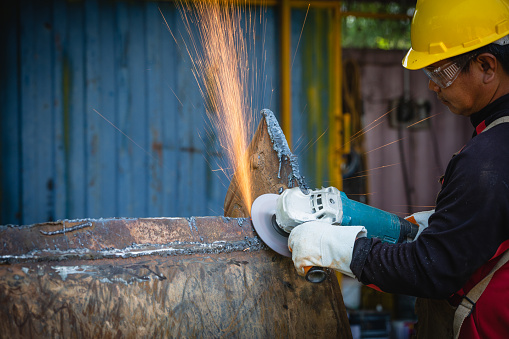 Male welder wearing helmet working with welding torch in factory.