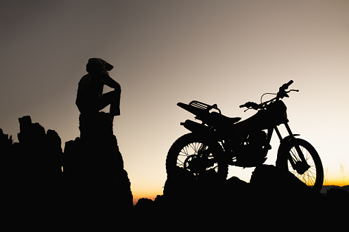 Man with motocross bike against beautiful lights, silhouette of a man with motocross motorcycle On top of rock high mountain at beautiful sunset, enduro motorcycle travel concept.
