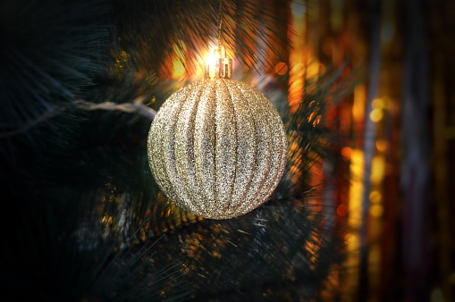 Christmas decoration - Closeup of one golden disco ball hanging in tree with lights in the backdrop