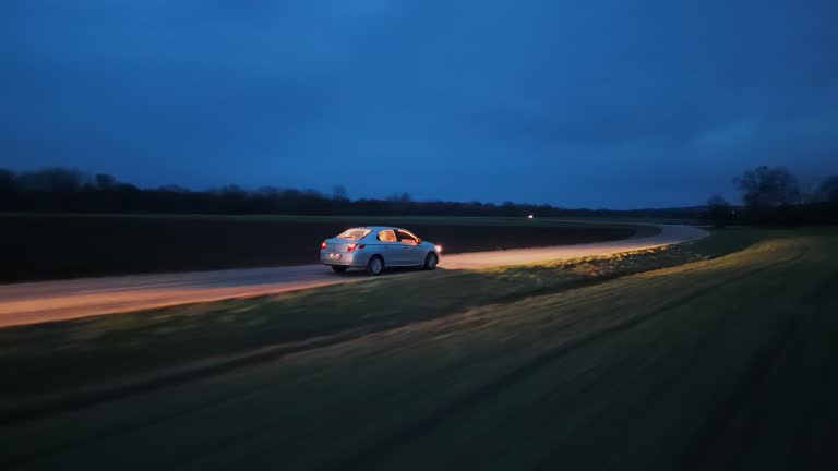 Drone Shot of Car With Glowing Headlights Driving Through Country Road Under Sky at Night