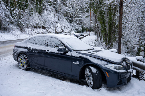 Portland, OR, USA - Feb 23, 2023: A BMW 535i sedan is seen abandoned on the hilly Highway 43 after skidding sideways and hitting the roadside guardrail during overnight snow storm in Portland, Oregon.