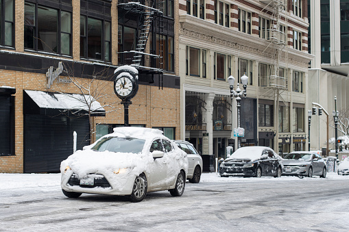 Portland, OR, USA - Feb 23, 2023: Snow-covered car driving on icy winter road in downtown Portland, Oregon, after overnight snow storm.