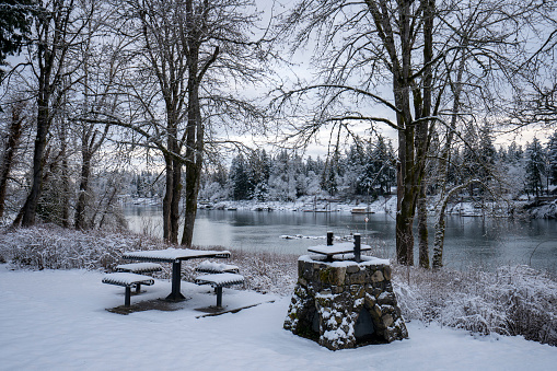 Snow-covered outdoor picnic table and fire pit in a park in Lake Oswego, Oregon, overlooking the Willamette River, on a cold winter morning after overnight snowfall.