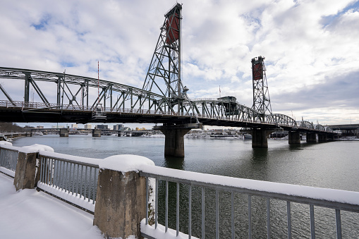 Hawthorne Bridge viewed from the west bank of the Willamette River in Portland, Oregon, after snowfall in winter. The truss bridge is the oldest vertical-lift bridge in operation in the United States.