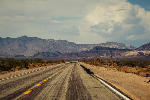 A car driving on a desert road against mountains, with a cloudy sky overhead in the United States