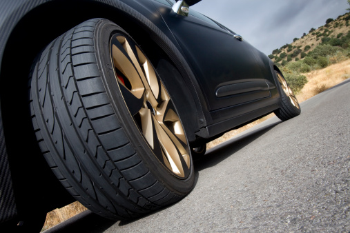 Close view of the wheel of a black sport car with the asphalt at foreground